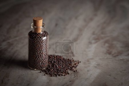 Photo for A small glass bottle filled with organic Black mustard seed (Brassica nigra) is placed on a marble background. - Royalty Free Image