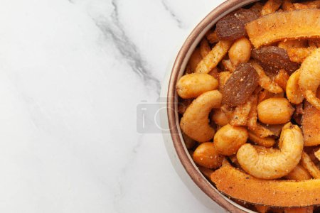 Nahaufnahme von Shahi vrat oder upvas oder Fasten namkeen Mischung aus Kokos, gemahlenen Nüssen, Cashew, Kartoffelscheiben, Erdnüssen, indischen würzigen Snacks (Namkeen), serviert in Keramikschüssel über weißem Granithintergrund