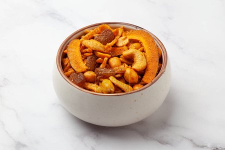 Close-up of  Shahi vrat or upvas or Fasting namkeen Mixture made from coconut,ground nuts, cashew, potato slice, peanut, Indian spicy snacks (Namkeen), served in ceramic bowl over white granite  background