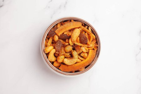 Close-up of  Shahi vrat or upvas or Fasting namkeen Mixture made from coconut,ground nuts, cashew, potato slice, peanut, Indian spicy snacks (Namkeen), served in ceramic bowl over white granite  background