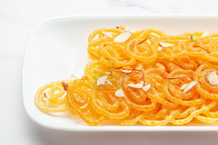 Close-Up of Indian Classical  Sweet Jalebi . Garnished with kesar (Saffron) and dry nuts, Jalebi is one of the most delicious sweets widely used in India. Selective Focus, Selective Focus on Subject, Background Blurred white .