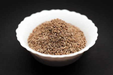 Organic Cumin seed (Cuminum cyminum) in white ceramic bowl on dark background.
