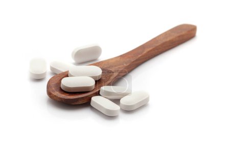 Health care concept. A wooden spoon filled with white colored Tablets. Isolated on a white background.