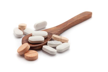 Health care concept. A wooden spoon filled with multi-colored Tablets. Isolated on a white background.