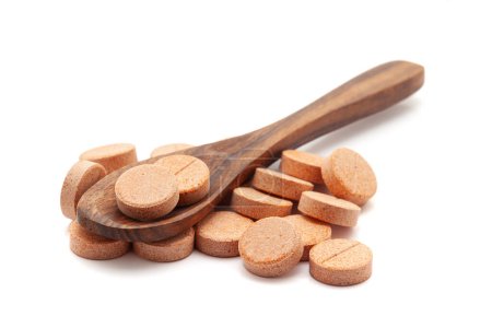 Concepto de salud. Una cuchara de madera llena de píldoras y tabletas médicas de color naranja. Aislado sobre un fondo blanco.