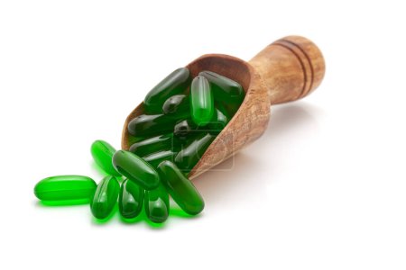 Concept de soins de santé. Une cuillère en bois remplie de capsules médicales de vitamine E (verte). Isolé sur fond blanc.
