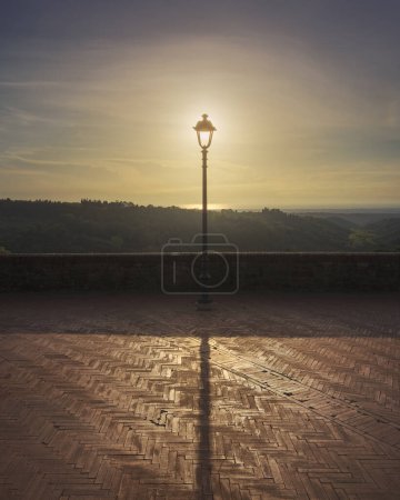 Photo for Lamp post on the Montescudaio terrace. Sun in the center and sea in the background. Province of Pisa, Tuscany region, Italy - Royalty Free Image