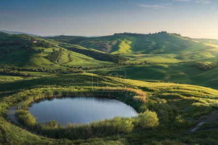 Small lake in the rolling hills of the Crete Senesi at sunset. Spring landscape in Monte Sante Marie, Asciano, Province of Siena, Tuscany region, Italy