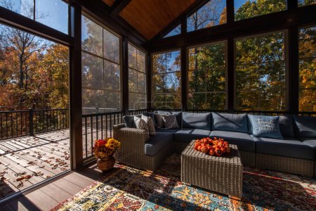 Photo for Cozy screened porch enclosure with contemporary furniture at Thanksgiving Holiday. Porch door open, flower bouquet in a vase, autumn leaves and woods in the background. - Royalty Free Image