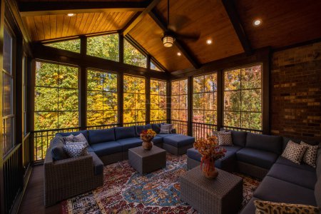 Photo for Cozy screened porch enclosure with contemporary furniture at Thanksgiving Holiday. Flower bouquet in a vase, autumn leaves and woods in the background. - Royalty Free Image