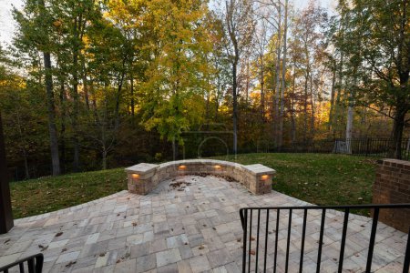 Pintoresca vista del patio trasero en la temporada de otoño con adoquines de patio y pared de piedra, hojas de otoño y maderas coloridas en el fondo.