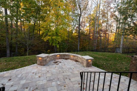 Photo for Picturesque backyard view in autumn season with patio pavers and stone wall, autumn leaves, and colorful woods in the background. - Royalty Free Image