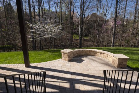 Picturesque backyard view in spring season with patio pavers and stone wall, blooming white cherry tree, and spring colored woods in the background.