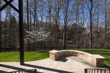 Vue pittoresque sur la cour arrière au printemps avec pavés patio et mur de pierre, cerisier blanc en fleurs et bois de couleur printemps en arrière-plan.