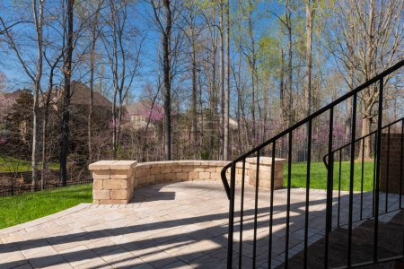 Picturesque backyard view in spring season with patio pavers and stone wall, blooming white cherry tree, and spring colored woods in the background.