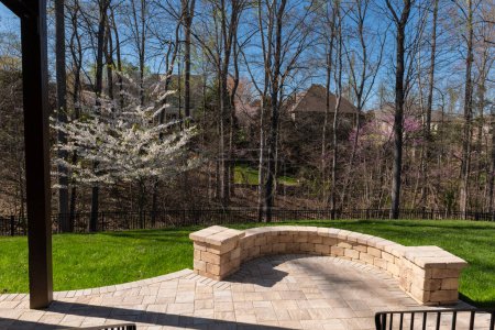 Vista del patio trasero en temporada de primavera con adoquines de patio y pared de piedra, cerezo blanco floreciente, y maderas de color primavera en el fondo.