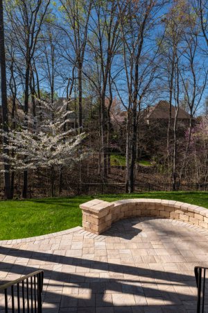 Photo for Picturesque backyard view in spring season with patio pavers and stone wall, blooming white cherry tree, and spring colored woods in the background. - Royalty Free Image