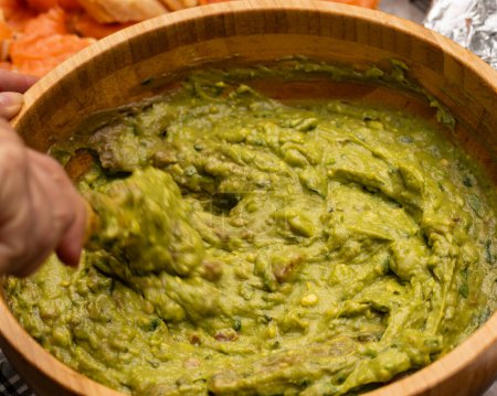 Mixing freshly homemade guacamole in a wooden bowl. Party catering concept.