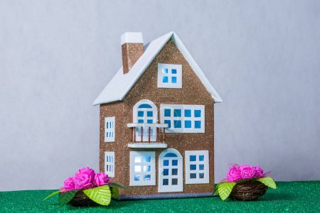 There are flowers near a brown toy house with blue light in the windows