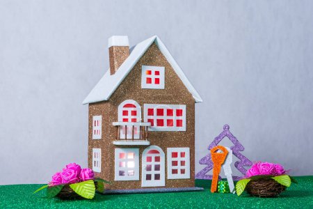 Près d'une maison de jouets marron avec de la lumière rouge dans les fenêtres, il y a des fleurs et un arbre de Noël avec des clés