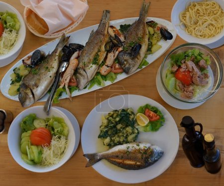 Photo for Appetizing seafood as lunch .Langoustines , red mullet, sea bass grilled with lemon, potato  ,shellfish ,pasta ,bread, sauce and salad on the table in the restaurant , Croatia - Royalty Free Image
