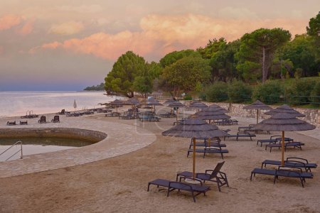 Téléchargez les photos : Beach and resort with beach chairs and umbrellas  in morning light on the beach of a Croatian seaside holiday resort in Porec, Istria, no people.Traveling concept background - en image libre de droit