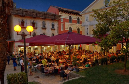 Foto de POREC, CROATIA - September 07, 2021: Many tourists are relaxing in an open-air bar at night, Porec, Unesco, Croatia. Travel destination. Summer vacation. Illustrative editorial - Imagen libre de derechos