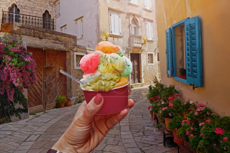 Foto de Mujer de la mano sostienen hermoso hielo dulce brillante - cono de crema con diferentes sabores en la mano en el fondo de la antigua calle en Porec, Croacia. Concepto de viaje fondo - Imagen libre de derechos