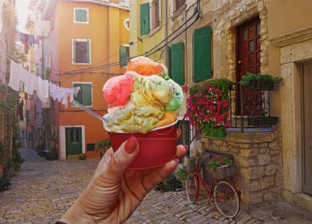 Téléchargez les photos : Woman hand hold  beautiful bright sweet ice - cream cone with different flavors  held in hand on the background of old street  in  Rovinj .Rovinj is a tourist destination on Adriatic coast of Croatia - en image libre de droit