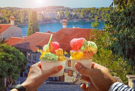 Photo for Couple with beautiful bright sweet ice cream of different flavors in the hand.Background of   view of the see and old street  in  Rovinj .Rovinj is a tourist destination on Adriatic coast of Croatia.Traveling concept background - Royalty Free Image