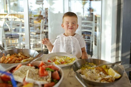 Foto de Me alegra que un niño pequeño coma mariscos en un restaurante. Dieta mediterránea. Comida saludable para niños. Pescado de mar para el almuerzo como fuente de yodo. Un niño en un café está comiendo. - Imagen libre de derechos