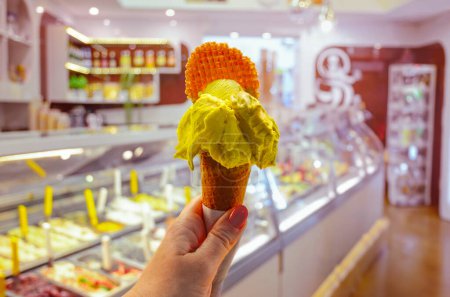 Téléchargez les photos : Glace italienne - cône de crème tenue à la main sur le fond de la boutique à Rome, Italie. C'est l'un des meilleurs endroits de crème glacée de la ville populaire parmi les touristes - en image libre de droit