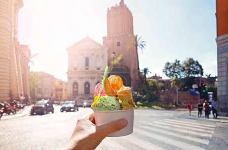 Foto de Cono de helado de helado dulce brillante italiano con diferentes sabores tomados de la mano en el fondo de la Piazza en Roma, Italia - Imagen libre de derechos