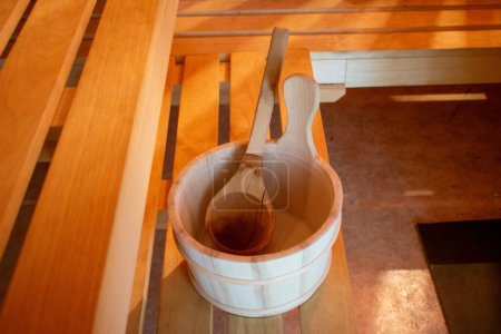 Wooden sauna bucket with wooden ladle in warm light.