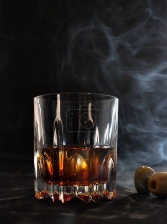 Téléchargez les photos : Verre à whisky sur un comptoir de bar avec fumée et olives. photo basse clé - en image libre de droit