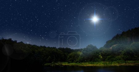 Bright star indicates the Nativity of Jesus Christ in the starry sky. Fog is rising over the night forest