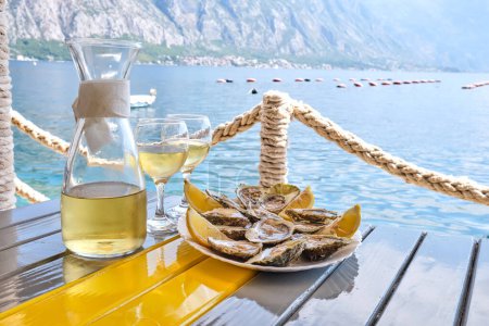 Téléchargez les photos : Huîtres et vin blanc dans un restaurant avec vue sur la mer. - en image libre de droit