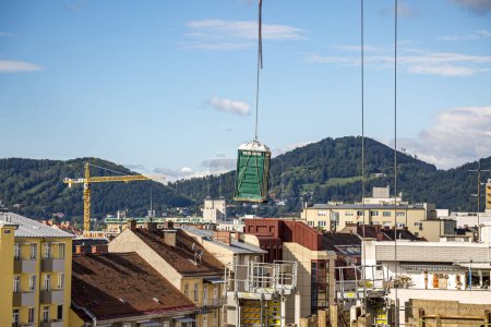 Photo for Crane lifted a chemical toilet at a construction site against a blue sky in Graz, Austria. - Royalty Free Image