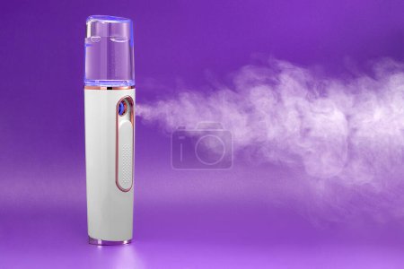 Frontansicht des Dampfes aus einem tragbaren Luftbefeuchter auf violettem Hintergrund. Schönheitsbehandlung des Gesichts im Schönheitszentrum.