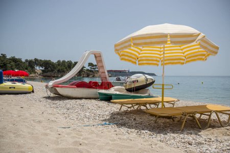 A relaxation area on the beach. Two chaise lounges with soft mattresses stand on the sand in the shade of a sun umbrella. Near them there are water bikes waiting for beachgoers.