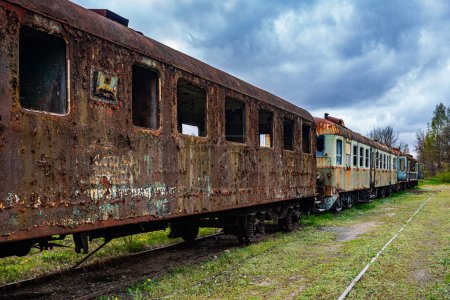 Téléchargez les photos : Ancien wagon de voyageurs rouillé avec plusieurs unités électriques abandonnées sur le terrain du cimetière ferroviaire - en image libre de droit
