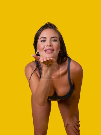 Photo for Glad female model in underwear smiling and blowing air kiss to camera against yellow background - Royalty Free Image
