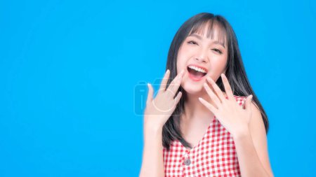 Téléchargez les photos : Portrait de belle femme asiatique mignonne fille en robe rouge avec la frange coiffure, rire et sourire de bonne humeur isolé fond bleu avec espace de copie - en image libre de droit