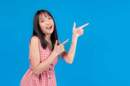 Foto de Hermosa mujer asiática linda chica con estilo de pelo flequillo en camiseta azul sonriendo y señalando con el dedo al espacio de copia vacío para el producto actual o espacio en blanco para la publicidad aislada en fondo azul - Imagen libre de derechos