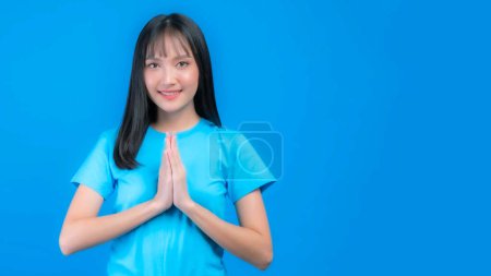 Téléchargez les photos : Portrait belle asiatique jeune femme frange coiffure payer le respect, sawasdee symbole de la Thaïlande saluant la culture pour bonjour ou au revoir isolé sur fond bleu - en image libre de droit