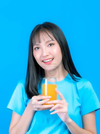 Téléchargez les photos : Beautiful beauty Asian woman cute girl with bangs hair style in blue shirt feel happy drinking orange juice for good health on  blue background with copy space - lifestyle beauty woman healthy concept - en image libre de droit