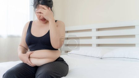 Téléchargez les photos : Asiatiques grosses femmes, Fat girl, Joufflu, en surpoids malheureux mesurer sa taille dans la chambre à coucher - Femme alimentation mode de vie problème de surpoids concept - en image libre de droit