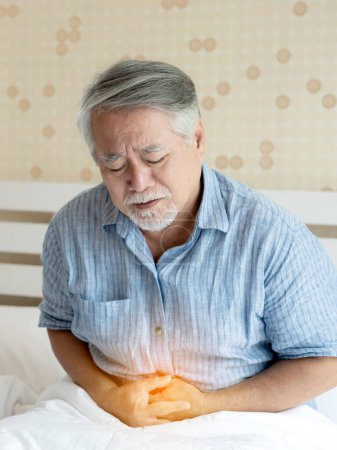 Téléchargez les photos : Senior mâle asiatique souffrant de mauvaise douleur dans son ont mal à l'estomac à la maison concept de soins de santé senior - en image libre de droit