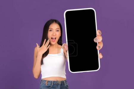 Photo for Full body length photo portrait of beautiful Asian young woman ,Excited surprised girl showing big smart phone with blank screen , white screen isolated on purple background , Mock Up Image - Royalty Free Image