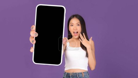 Téléchargez les photos : Portrait de belle jeune femme asiatique, Fille surprise excitée montrant un grand téléphone intelligent avec écran blanc, écran blanc isolé sur fond violet, Image maquillée - en image libre de droit